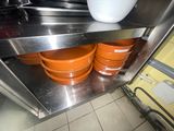 Plusieurs bols orange sont empilés sur une étagère en acier inoxydable dans une cuisine