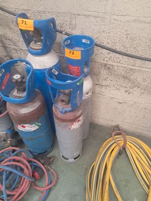 Plusieurs bouteilles de gaz propane et des tuyaux sont alignés contre un mur