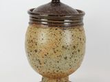 brown and white ceramic jar with lid on pedestal on white background