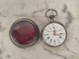une montre de poche en argent et une montre en verre rouge posées sur une surface en marbre