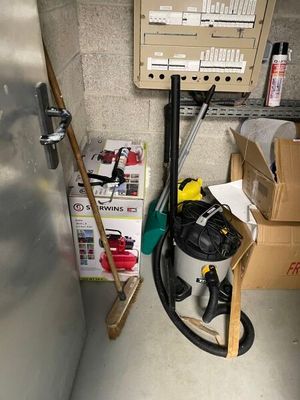a vacuum in the corner of a room next to boxes and a broom