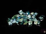 un gros plan sur un tas de diamants bleus et verts posés sur une surface noire