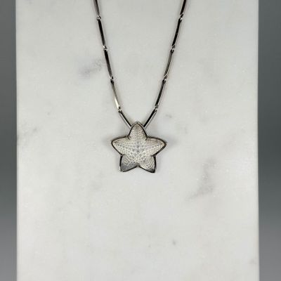 un collier en argent orné d'un pendentif en forme d'étoile, posé sur une surface en marbre blanc
