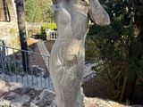 une statue représentant une femme tenant un chapeau, au sommet d'un mur de pierre