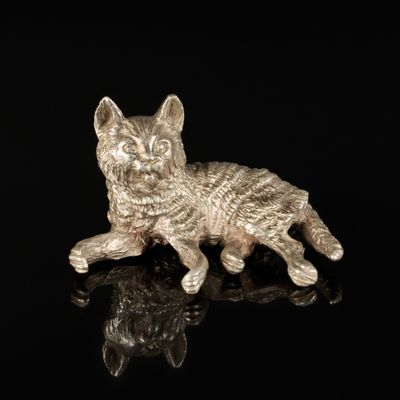 une figurine en argent représentant un chat, posée sur un fond noir