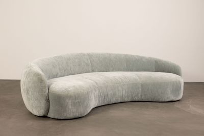 an image of a curved couch sitting on top of a cement floor
