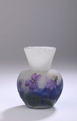 un vase en verre orné de fleurs violettes, posé sur une surface blanche