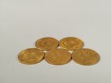 five gold coins sitting on top of each other on a white surface
