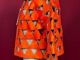 an orange jacket on a mannequin stand with a red background