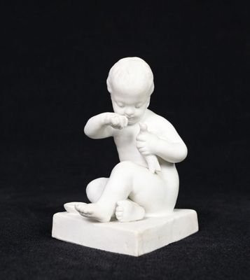 a small white statue of a boy sitting on a block