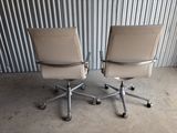pair of tan leather office chairs on casteors in front of a corrugated wall