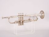 an old silver trumpet sitting on a clear stand on a white surface