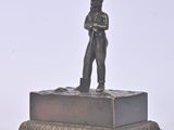 bronze figurine of a man standing on a pedestal with his arms crossed