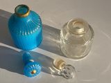 une bouteille en verre bleu avec un bouchon doré, à côté d'une bouteille en verre transparent avec un bouchon doré
