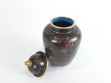 un petit vase muni d'un couvercle, posé sur une surface blanche