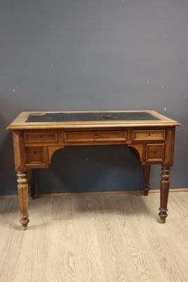 un vieux bureau en bois avec un plateau en verre, posé sur un parquet en bois massif