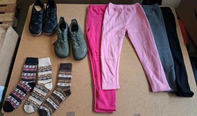 several pairs of shoes, socks, and leggings are laid out on a cardboard box