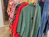 clothes hanging on a rack in a clothing store next to a mirror