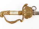 a gold colored sword with a carved handle on a white surface