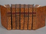 six antique books lined up in a row on a gray surface