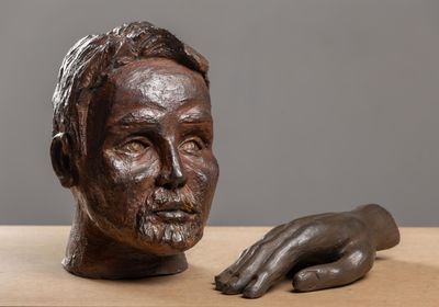 sculpture représentant la main d'un homme posée sur une table, à côté d'un buste d'homme