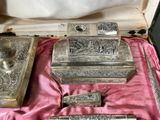 a silver box with silver items in it on a pink cloth