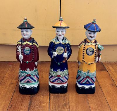 trois figurines en céramique représentant des hommes asiatiques debout sur un plancher en bois