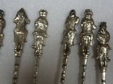 several silver metal figurines are lined up on a white surface
