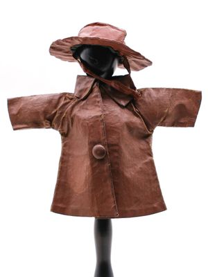 poupée vêtue d'un manteau en cuir marron et d'un chapeau, posée sur un socle noir