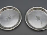 two silver plates with initials on them sitting on a table