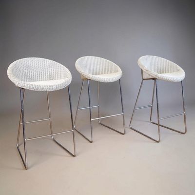 three white wicker bar stools with chrome legs against a gray wall