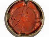 a red piece of wax in a tin on a white surface