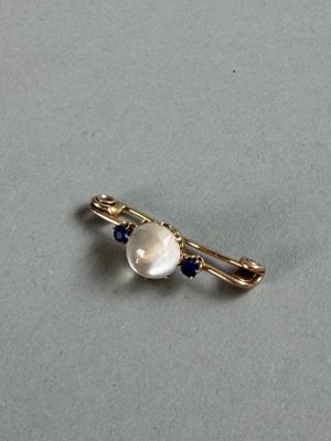 a close up of a pearl and sapphire broochle on a gray surface