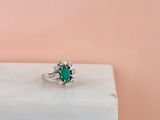 a close up of a green emerald and diamond ring on a white marble block