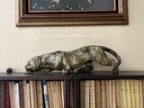 a statue of a cat on a book shelf in front of a painting