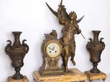 une horloge posée à côté de trois vases et d'une statue
