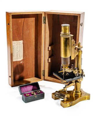 un microscope en or posé dans un coffret en bois, à côté d'une bague rose