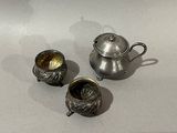 a silver tea pot and two silver cups on a table