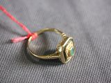 gold ring with green stone and red string on grey cloth