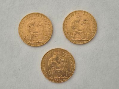 On voit trois pièces d'or sur une surface blanche