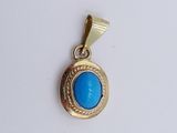 un gros plan d'un pendentif en or et en turquoise sur une surface blanche