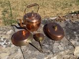 trois casseroles en cuivre et une bouilloire posées sur une dalle de pierre