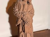 une statue représentant un homme tenant un enfant dans ses bras, posée sur un plancher en bois