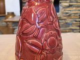 un vase rouge posé sur une table, avec un mur de pierre en arrière-plan
