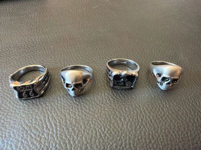 trois bagues en forme de crâne en argent posées sur une surface en cuir