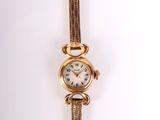 une montre-bracelet en or avec un cadran blanc sur une surface blanche