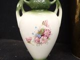 a white vase with a green handle and flowers on it