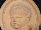 a clay picture of a baby on a plate next to a teddy bear