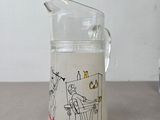 a glass pitcher with a drawing on it sitting on a table