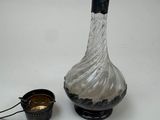 une bouteille en verre avec une poignée noire, à côté d'un petit récipient en métal